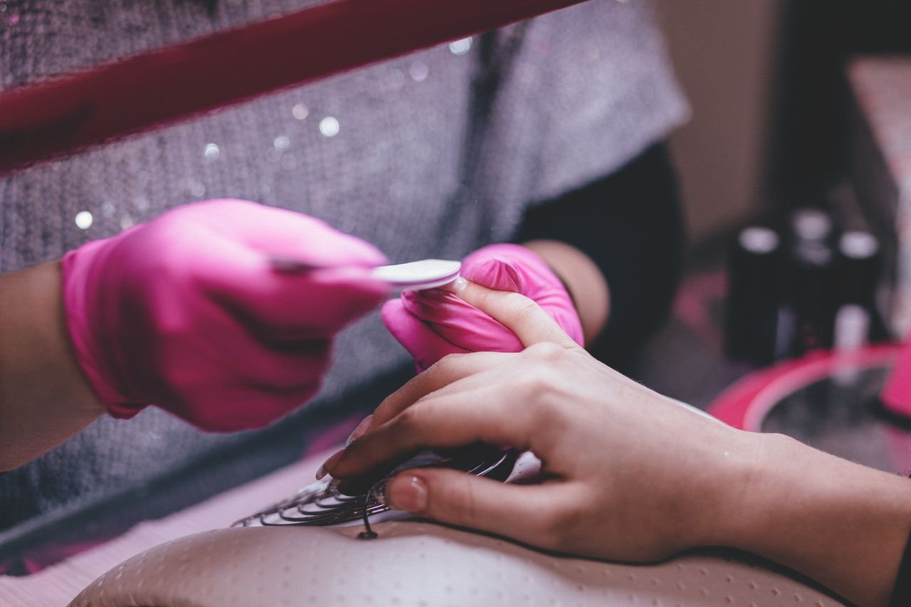 Services Close-up of a professional manicure session with pink gloves and a nail file in an indoor salon.